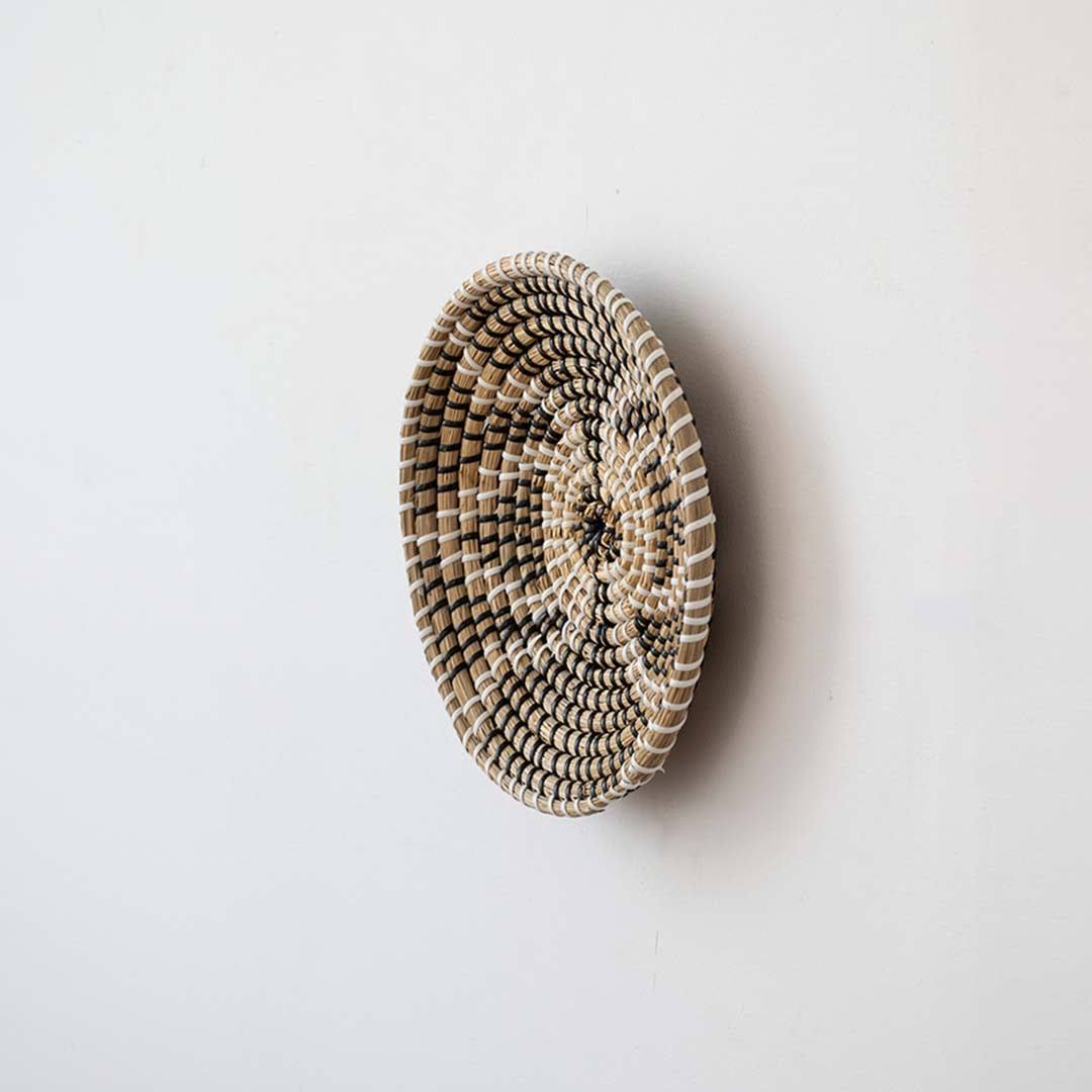 Side angle view of a butterfly pattern black woven seagrass wall hanging basket plate showing depth on a white wall.