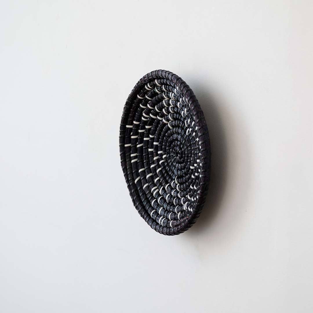 Side angle view of a star pattern black woven seagrass wall hanging basket plate showing depth details on a white wall.
