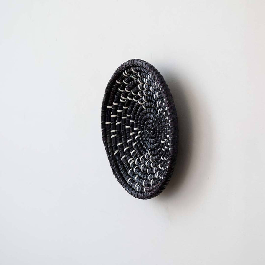 Side angle view of a star pattern black woven seagrass wall hanging basket plate showing depth details on a white wall.