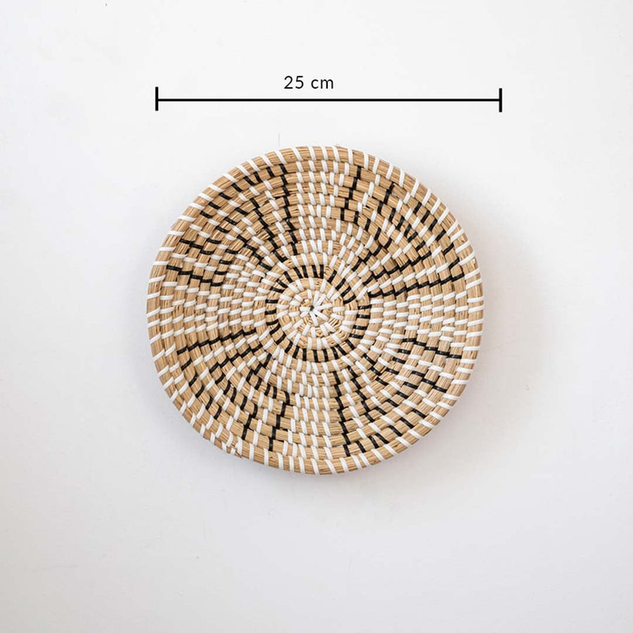 Handwoven wall basket in natural and black fiber shown with 25cm diameter for decorative wall placement.