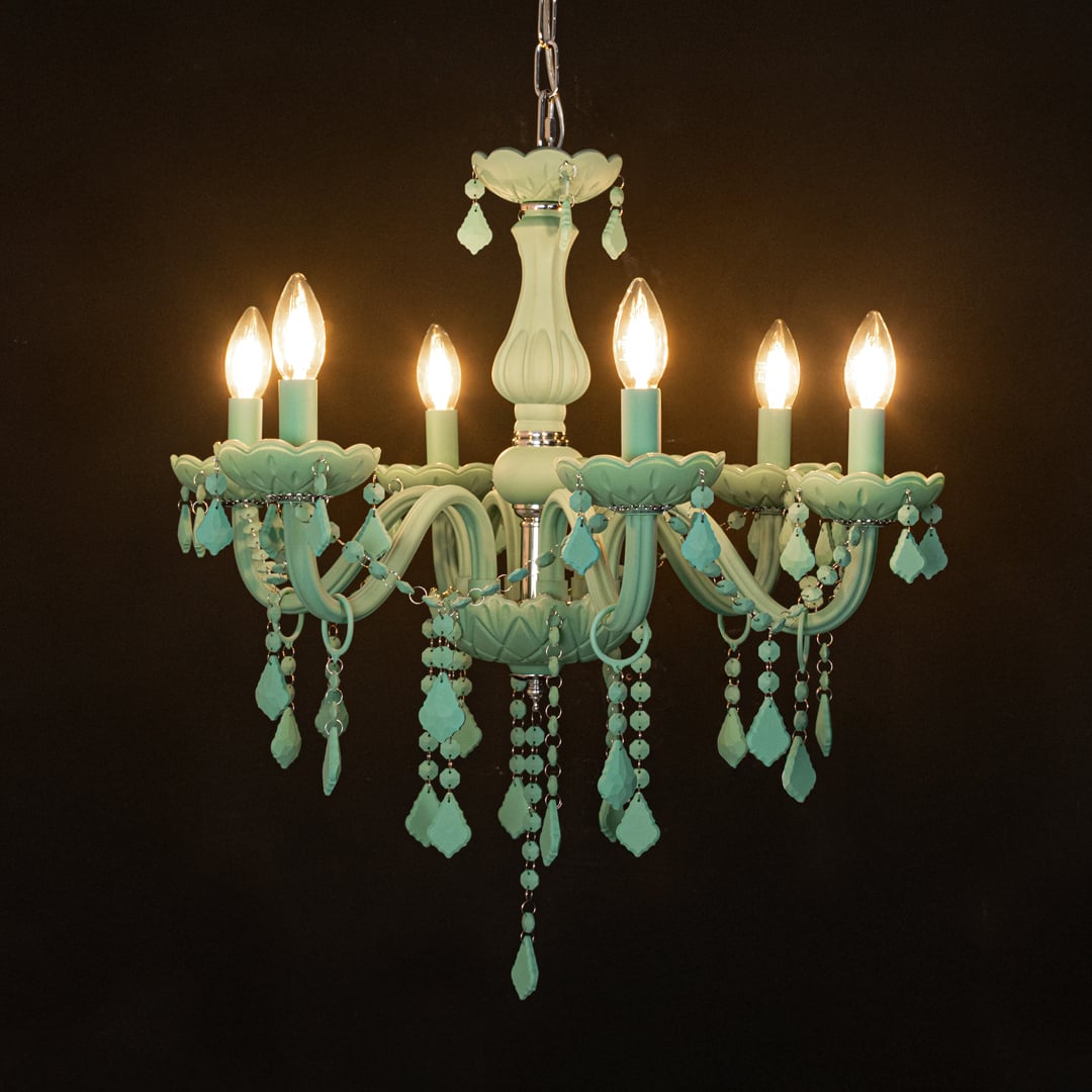 Green crystal chandelier glowing warmly on black background creating a striking luxury ceiling feature.