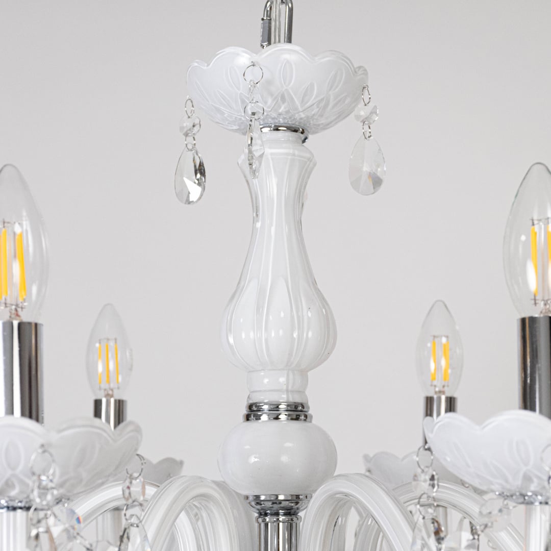 Closeup of white chandelier with crystal accents showing detailed arms and hanging droplets for decor style.