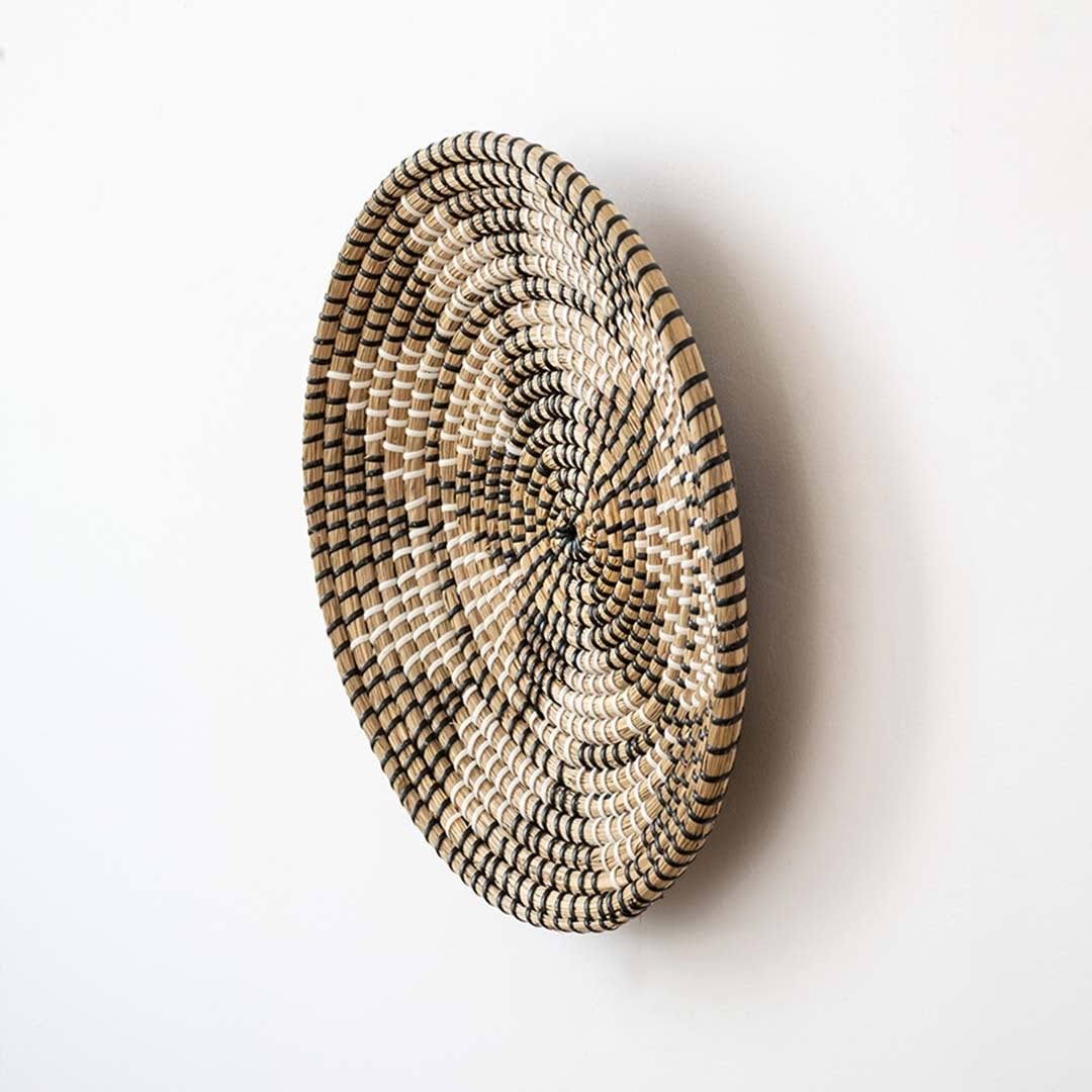 Handwoven seagrass round wall basket decor in natural beige and black with raised woven profile displayed on white background.