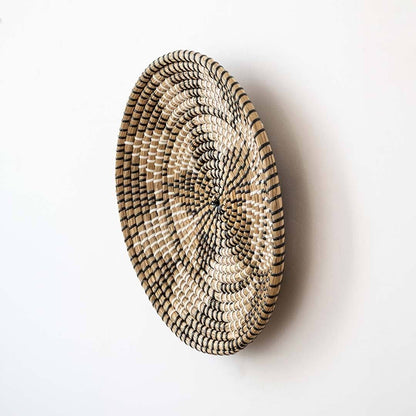 Handwoven seagrass round wall basket decor in natural beige and black with raised woven profile displayed on white background.