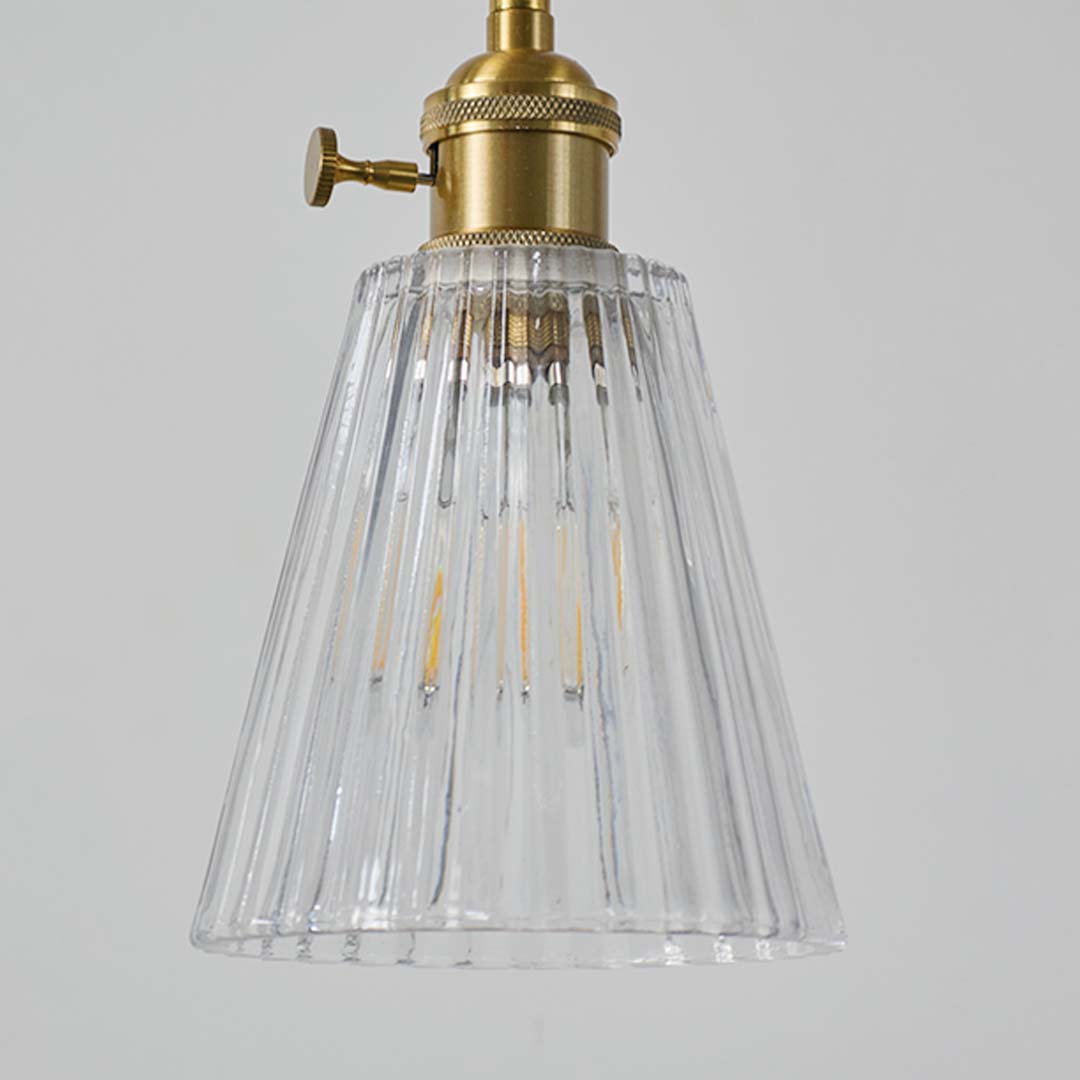 Closeup of clear ribbed glass pendant light showing brass fitting and warm bulb glow for contemporary home interiors.