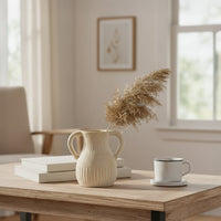 Twin handle vase styled on a wooden table with books and a coffee cup in a cozy minimal living room setup.