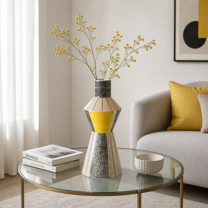Silver and yellow metal flower vase with dried stems placed on glass table for modern decor styling.