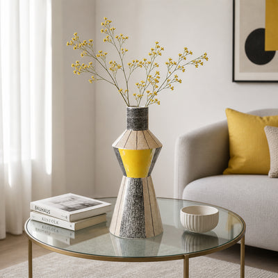 Silver and yellow metal flower vase with dried stems placed on glass table for modern decor styling.