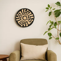 Large black and beige woven wall basket hanging on a white wall above a green armchair for modern boho living room decor styling.
