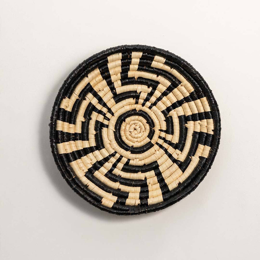Round woven black and cream seagrass wall basket with geometric sunburst labyrinth pattern on white background product image.
