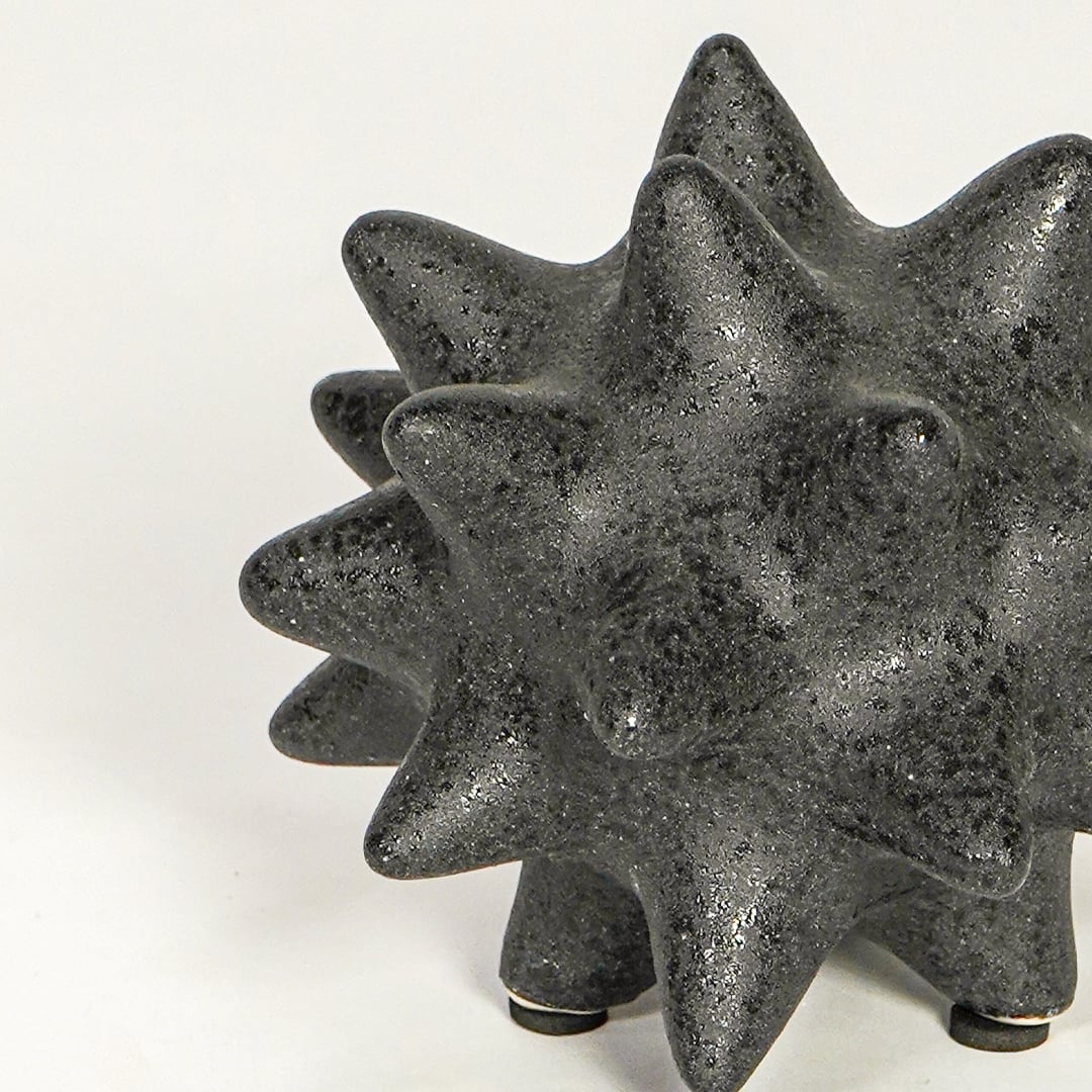 Close view of black ceramic decorative object highlighting rough textured finish and bold geometric spiked design.