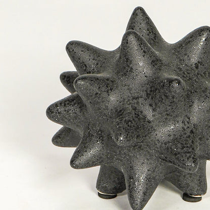 Close view of black ceramic decorative object highlighting rough textured finish and bold geometric spiked design.