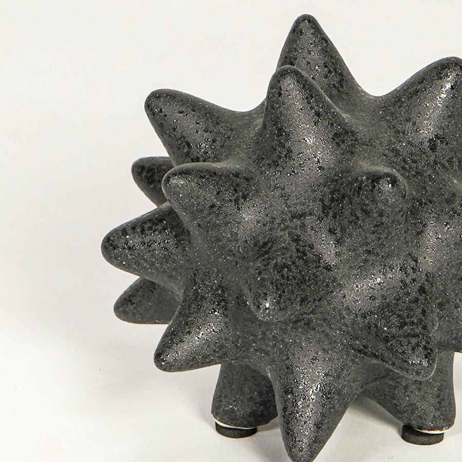 Close view of black ceramic decorative object highlighting rough textured finish and bold geometric spiked design.