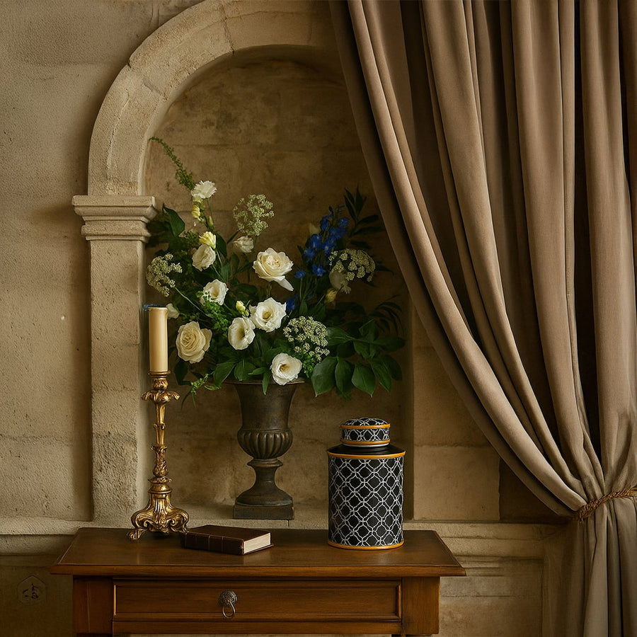 Black patterned jar with gold rim displayed on a wooden table beside flowers and candle adding luxury to interior decor.