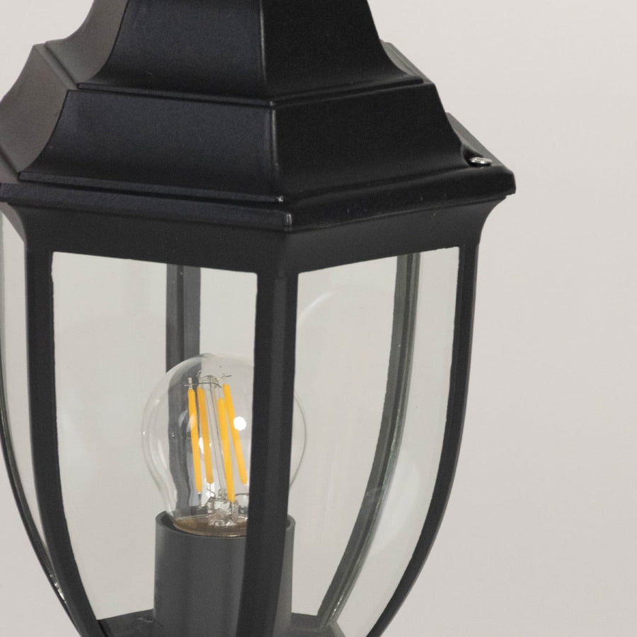 Closeup of outdoor black metal pillar lamp with clear glass panel highlighting LED bulb design and fine detailing.