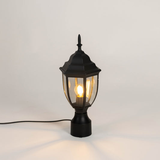 Black outdoor gate light with warm glowing bulb and clear glass shade for elegant exterior decor use.