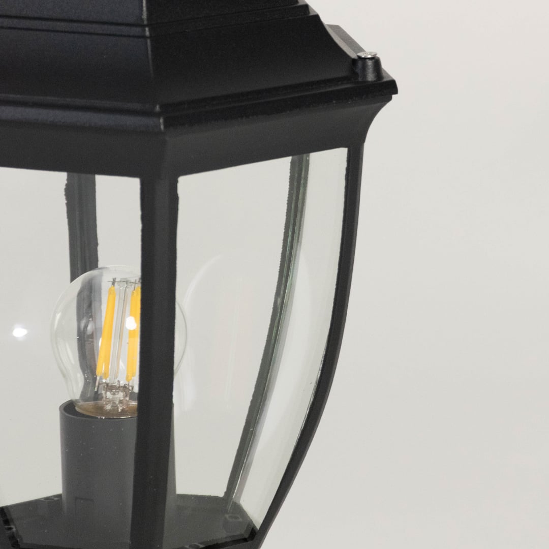 Closeup view of outdoor pillar light showing clear glass shade and bulb design framed in black matte metal housing.