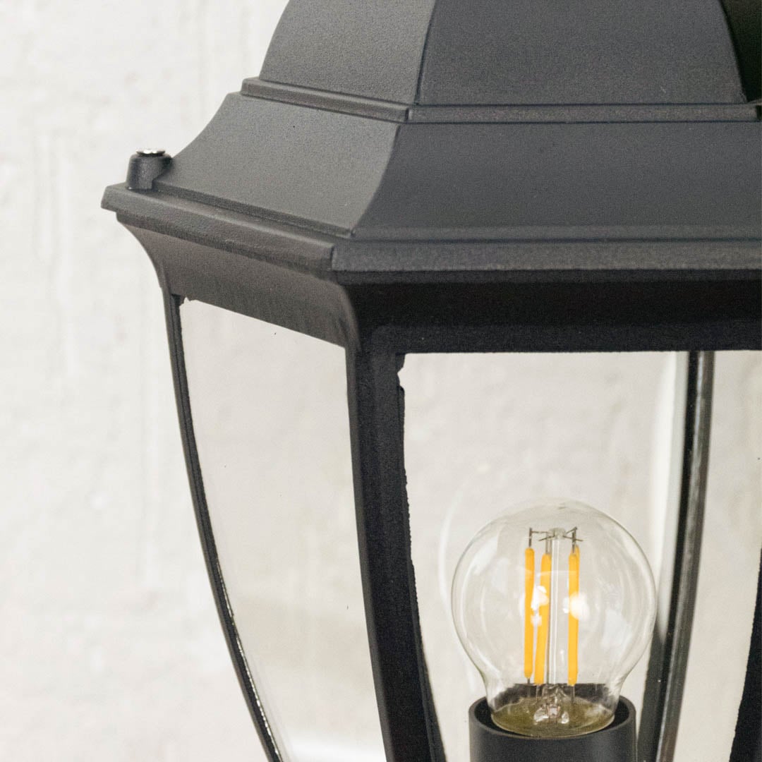 Detailed zoom of black outdoor pillar lamp highlighting transparent glass panels and visible LED bulb for decor.