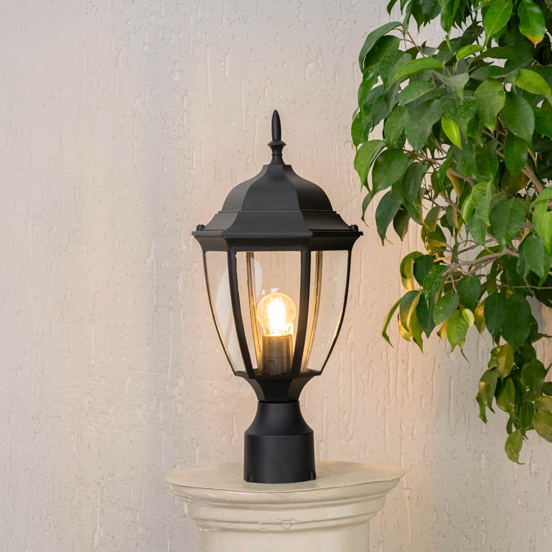 Outdoor black pillar lamp glowing with clear glass shade perfect for villa entrance terrace and landscaped garden use.