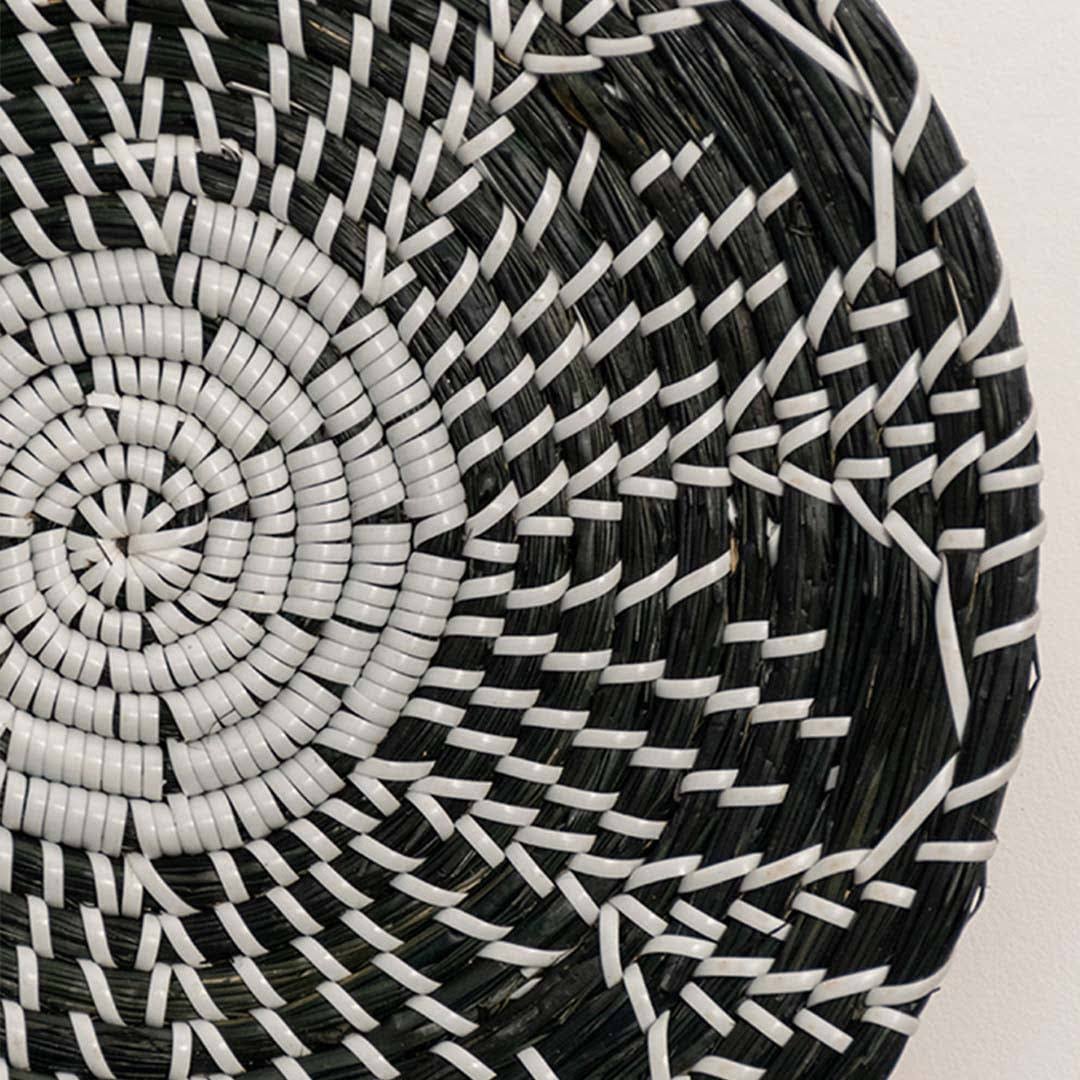 Detailed closeup of handcrafted black cream seagrass wall basket with woven geometric multi petal floral pattern home decor.