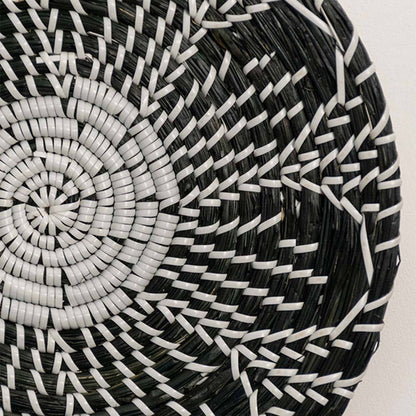 Detailed closeup of handcrafted black cream seagrass wall basket with woven geometric multi petal floral pattern home decor.