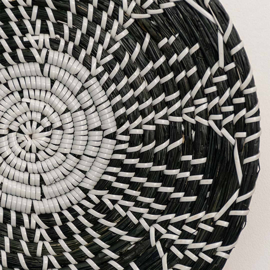 Detailed closeup of handcrafted black cream seagrass wall basket with woven geometric multi petal floral pattern home decor.
