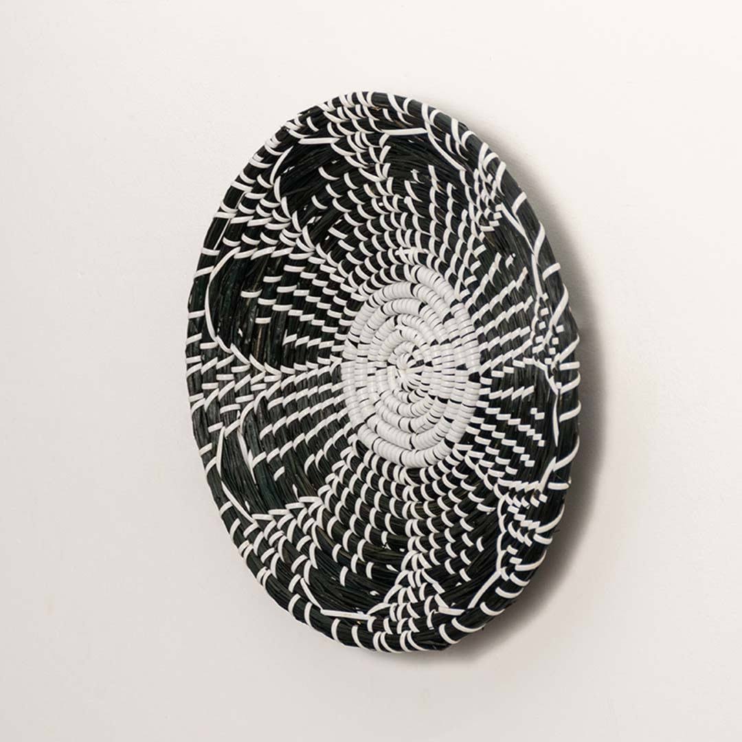 Side view of handcrafted black cream woven seagrass wall basket with detailed multi petal flower pattern for boho wall decor.