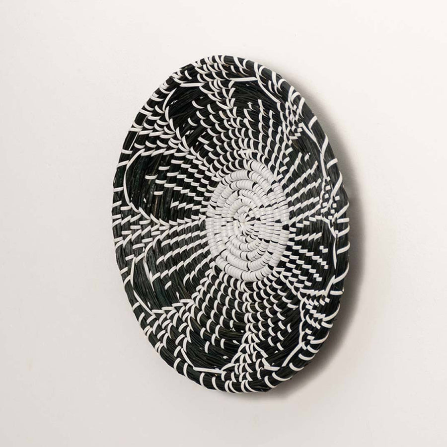 Side view of handcrafted black cream woven seagrass wall basket with detailed multi petal flower pattern for boho wall decor.