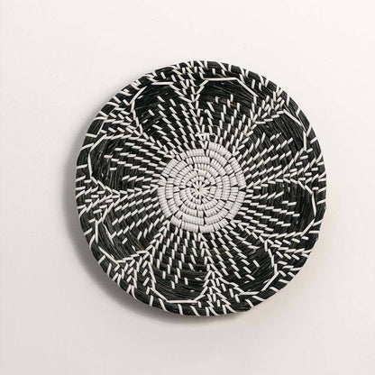 Round handcrafted black cream woven seagrass wall basket with detailed multi petal flower pattern on white background image.