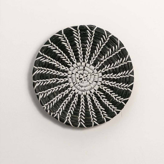 Round handcrafted black and white woven seagrass wall basket with starburst spoke design on white background product image.