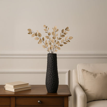 Tall black textured ceramic floor vase styled on wooden side table with dried leaves creating elegant modern living room decor.