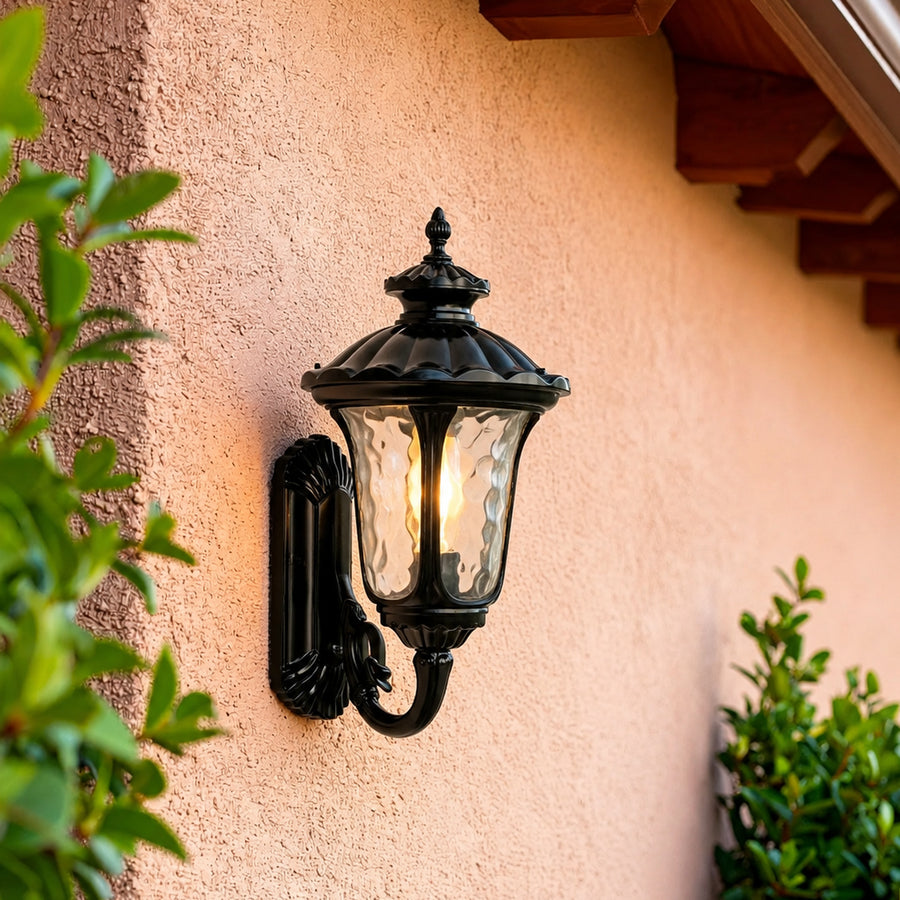 Classic black metal outdoor wall lantern lifestyle image with clear glass shade mounted on an orange stucco wall.