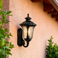 Classic black metal outdoor wall lantern lifestyle image with clear glass shade mounted on an orange stucco wall.