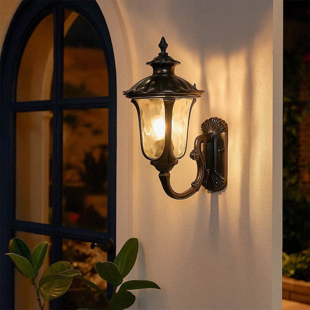 Elegant black outdoor wall lantern with curved arm and textured glass glowing warmly for porch and garden decor at home.