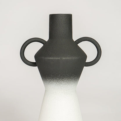 Closeup of black matte and white glazed ceramic vase with curved handles showcasing smooth ombre finish for home decor styling.