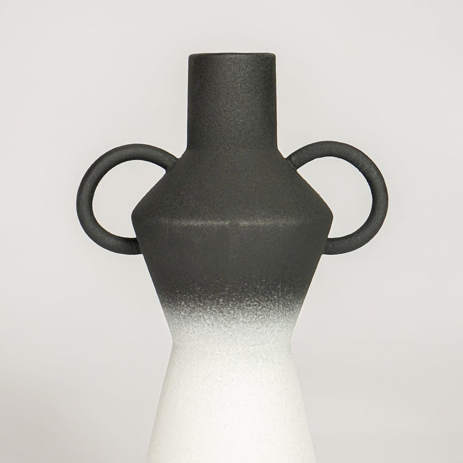 Closeup of black matte and white glazed ceramic vase with curved handles showcasing smooth ombre finish for home decor styling.