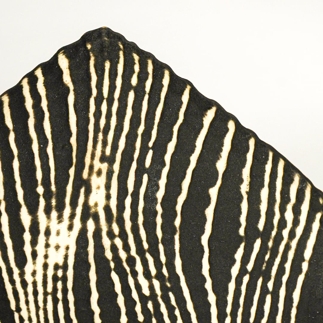 Closeup of black ceramic geometric decor object showing textured carved stripe pattern and matte artisan finish.