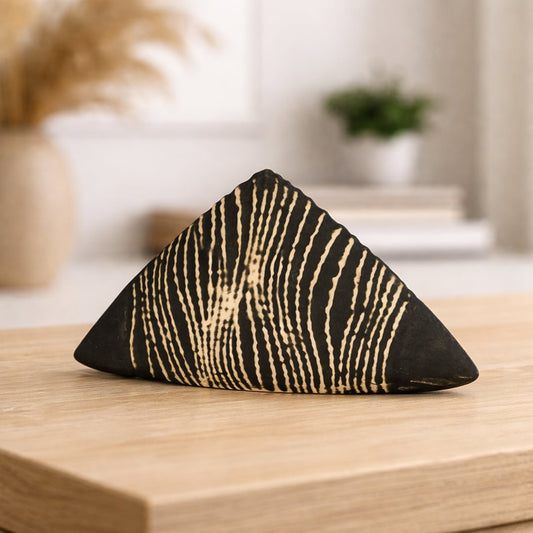 Black ceramic geometric decor object with carved stripe pattern placed on wooden table in modern neutral living room.