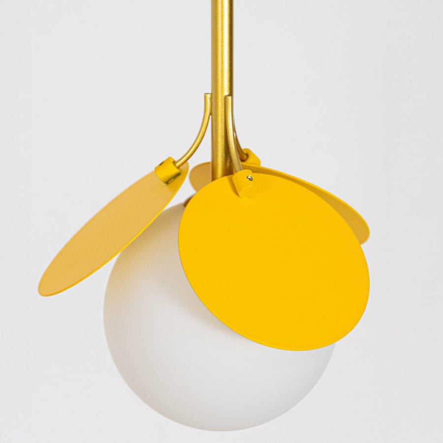 Closeup view of modern pendant light with frosted glass globe yellow metal petal accents and gold stem shown light off on white background.