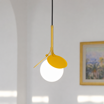 A modern pendant light with a matte yellow shade, a white globe bulb, and a gold metal stem suspended by a black cord in a bright, minimalist room.