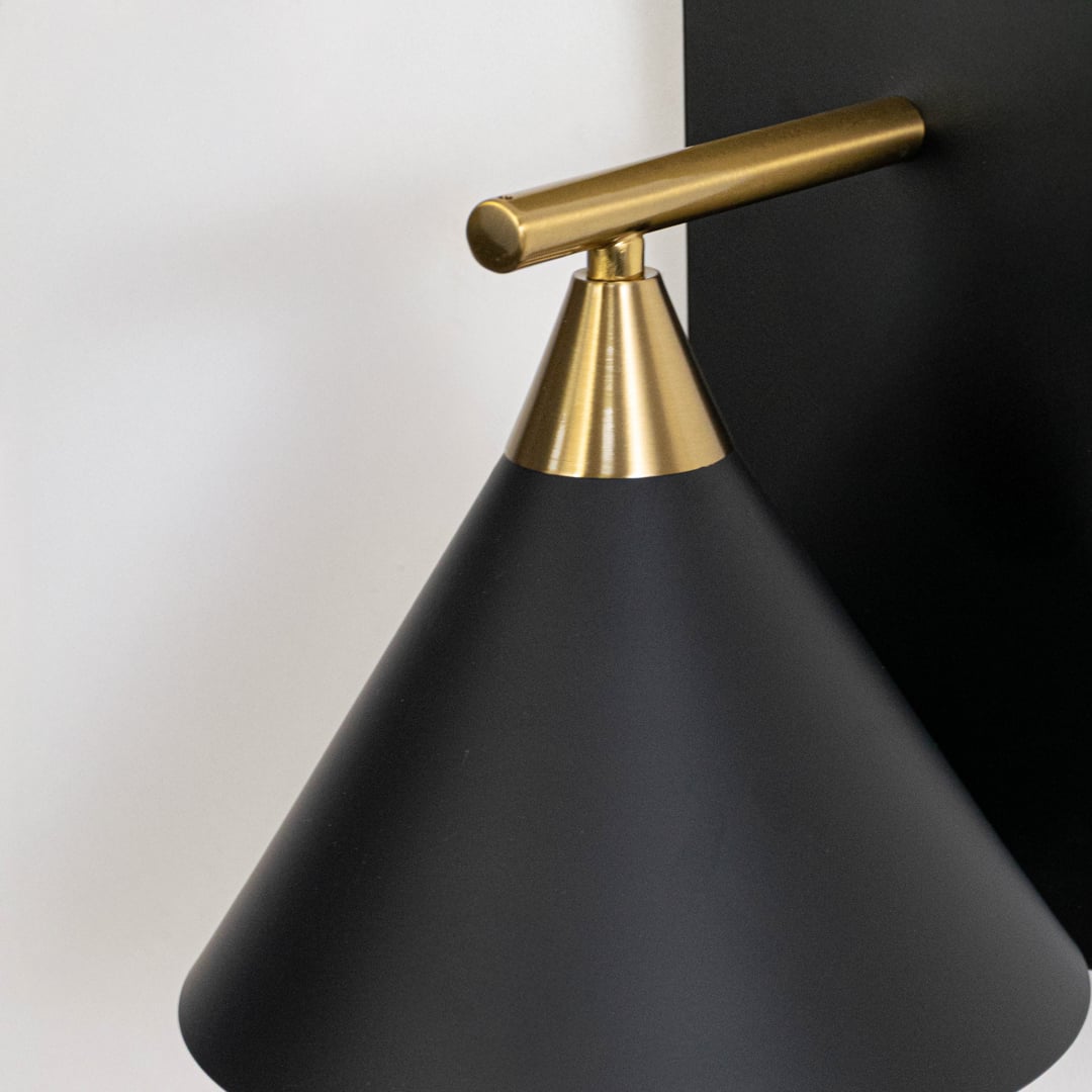 Detailed closeup of matte black metal cone shade and brushed brass gold arm on modern minimalist wall sconce light fixture.