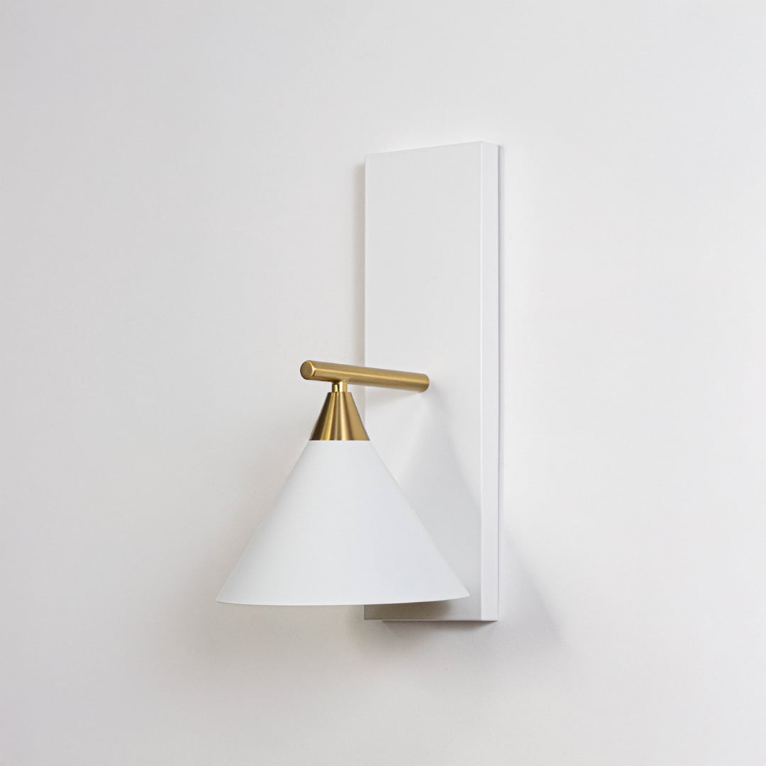 Contemporary white triangular shade wall light fixture with brass gold arm turned off on minimalist white background.