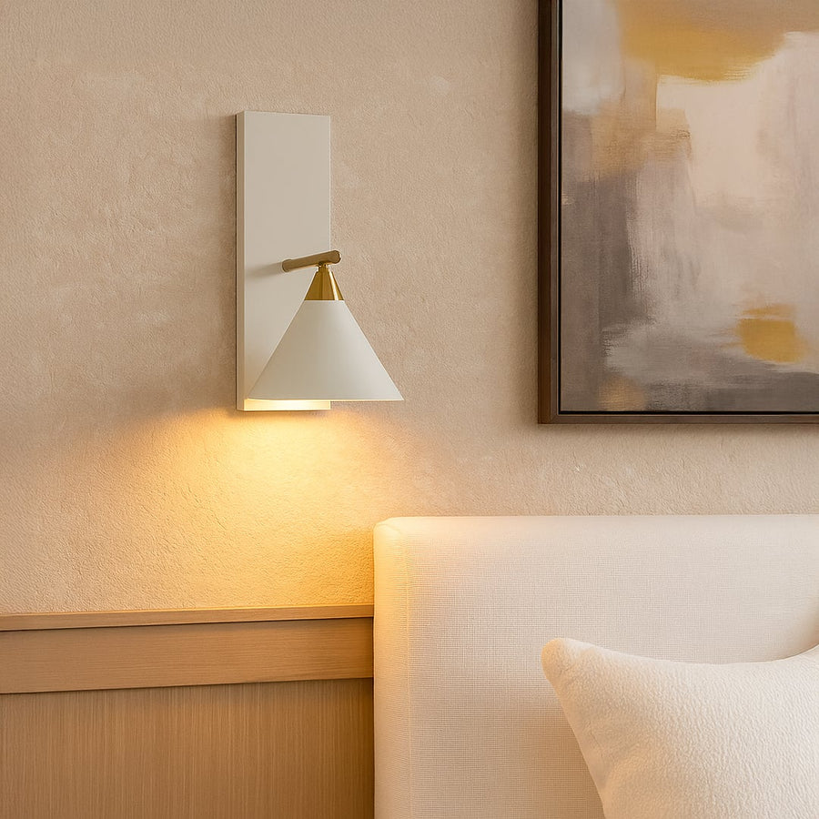Elegant white conical shade wall sconce with brass gold arm mounted on interior wall creating sophisticated ambient lighting.