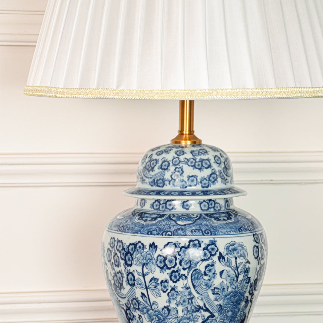 Closeup of blue white ceramic table lamp highlighting intricate floral detailing smooth glazed finish and gold metal base.