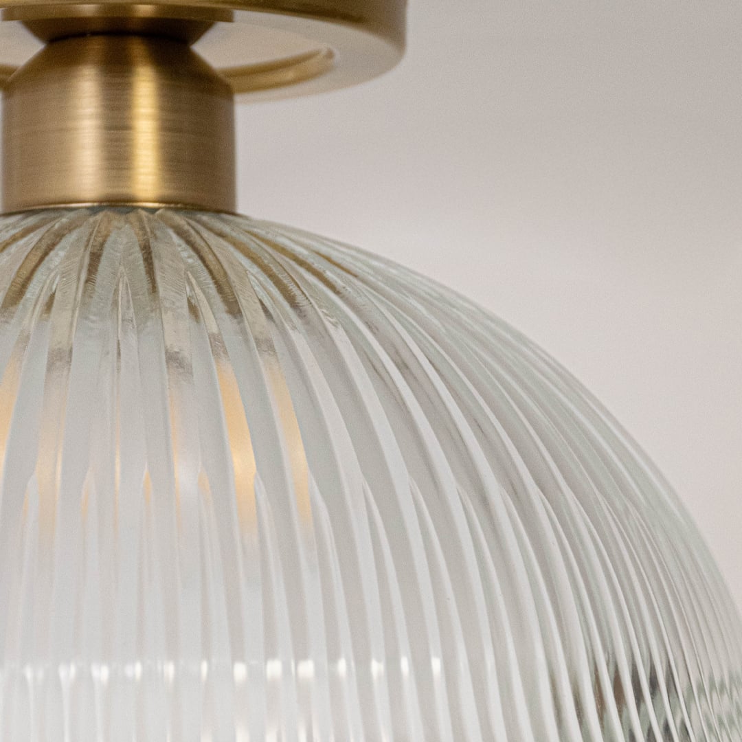 Closeup of ceiling light with brushed gold finish and ribbed clear glass dome shade for modern home lighting.