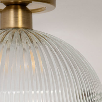 Closeup of ceiling light with brushed gold finish and ribbed clear glass dome shade for modern home lighting.