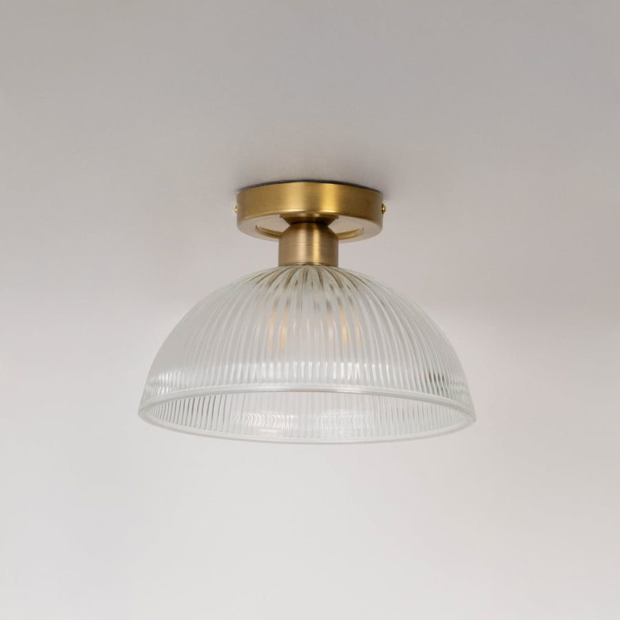 Ceiling light with brushed gold holder and ribbed clear glass dome shade shown switched off on plain white background.