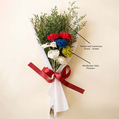 Red blue and yellow dried flower bouquet wrapped with green foliage and a red ribbon for luxury gifting on light backdrop.