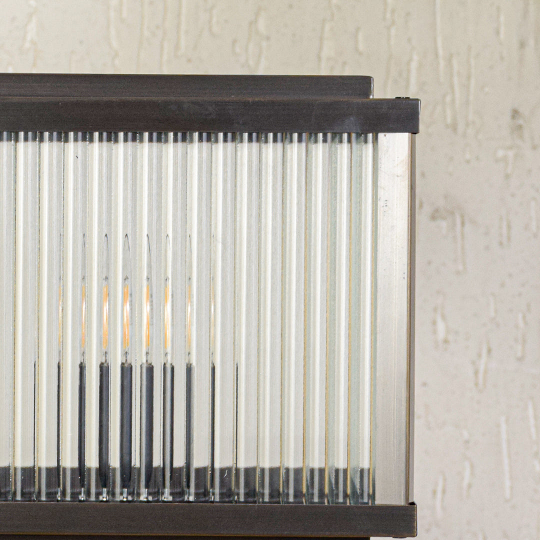 Close view of outdoor wall light with vertical ribbed glass panels and metal frame showcasing durable weather resistant lighting design.