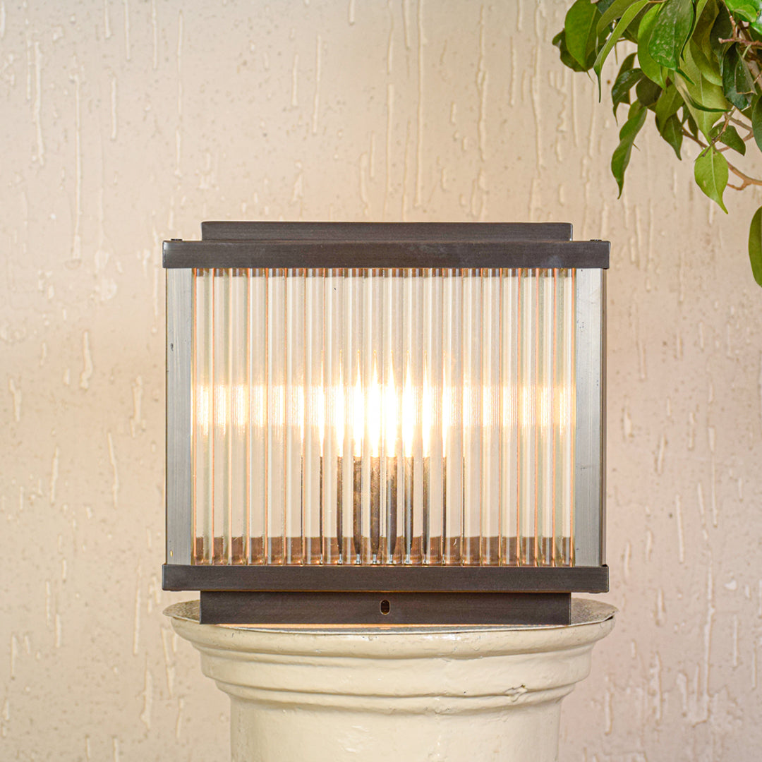 Contemporary outdoor wall light with ribbed glass shade mounted on exterior wall creating soft warm lighting for modern outdoor decor.

